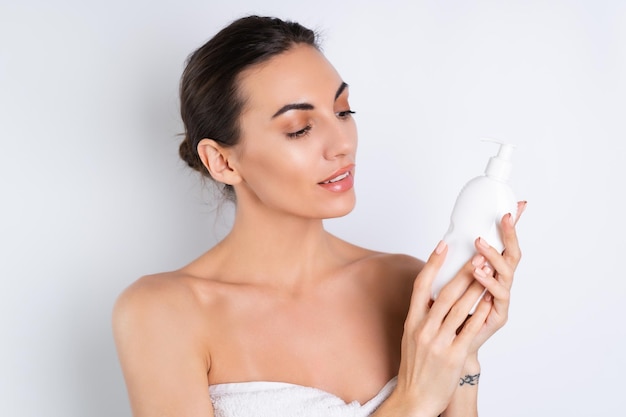 Close beauty portrait of a topless woman with perfect skin and\
natural makeup holding bottle of shampoo body lotion on a white\
backgroundx9