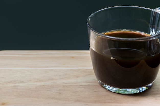 黒のコーヒーのガラスの左側に木製のボードとぼかし黒背景