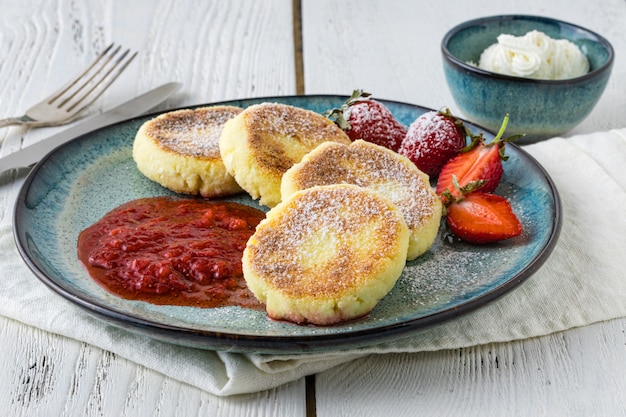 Close cheese pancakes, syrniki, curd fritters with fresh strawberries on plate table