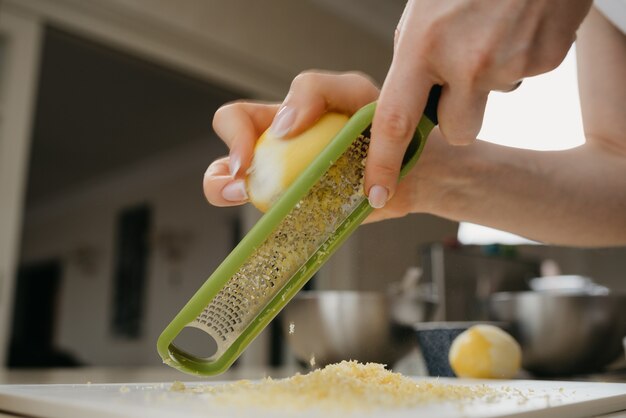 Una foto ravvicinata e dinamica dal basso delle mani di una giovane donna che separa la scorza di limone con una grattugia in cucina