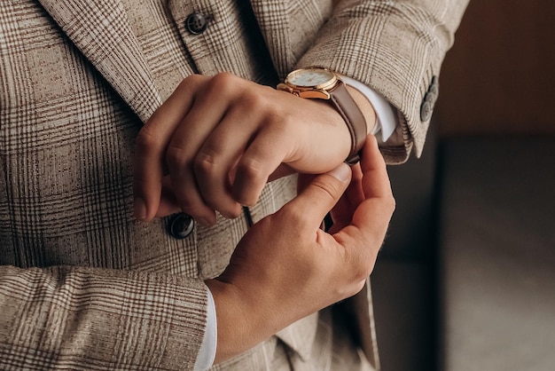 Close foto van details van de kleding van de man Ochtend van de bruidegom Stijlvolle man in een pak maakt een horloge vast aan zijn hand terwijl hij bij het raam staat