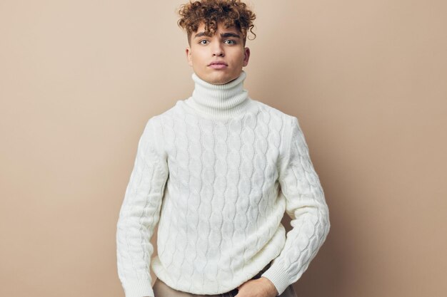 a close horizontal photo of a handsome attractive man standing in a white knitted sweater on a beige background looking at the camera