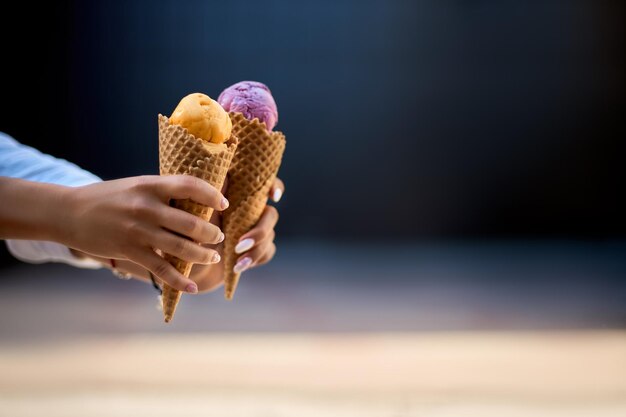 Close isolated view of two ice cream cones in hand of women friends standing outdoors no face