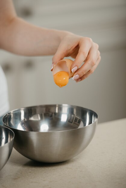 A close photo of the hand of a woman who is falling the yolk of the organic farm egg to the stainless steel soup bowl in a kitchen.