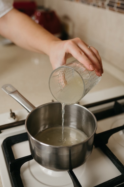 Photo a close photo of a hand of a woman who is pouring fresh lemon juice from the glass to the saucepan on the gas stove