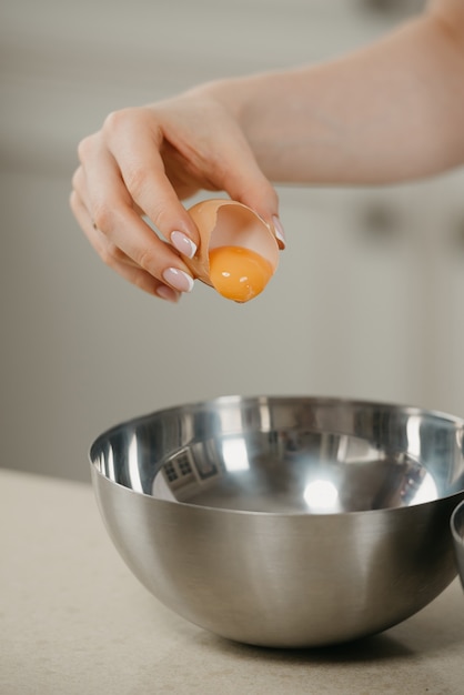 유기농 농장 달걀의 노른자를 부엌의 스테인리스 수프 그릇에 떨어 뜨리고있는 젊은 여성의 손 클로즈업 사진.