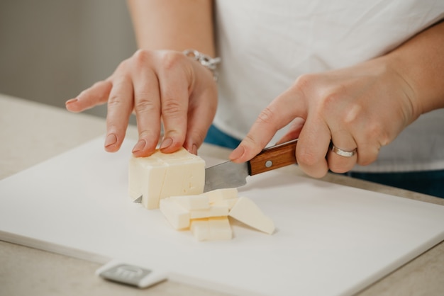 Ð close photo of the hands of a young woman who is cutting fresh butter on a cutting board with a sharp knife.