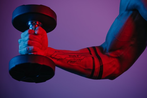 파란색과 빨간색 불빛 아래에서 아령으로 이두근 컬을하고있는 근육질 팔의 가까운 사진