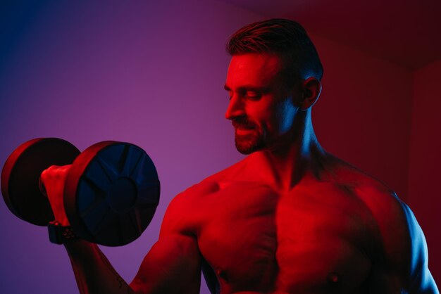 a close photo of a muscular man with a beard who is doing bicep curls with dumbbells under blue and red lights an athletic guy is demonstrating his sporty physique an athlete is training his arms