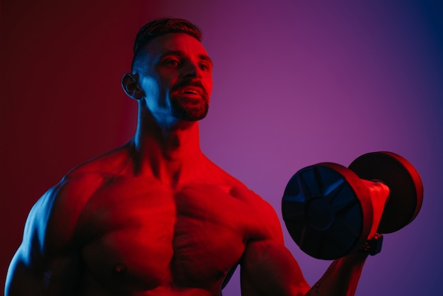 Una foto ravvicinata di un uomo muscoloso con la barba che sta facendo riccioli per bicipiti con manubri sotto luci blu e rosse