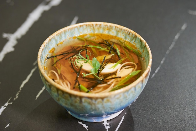 A close photo of traditional Japanese soup Ramen with egg pork nori pasta sesame in a blue ceramic bowl on a black stone table