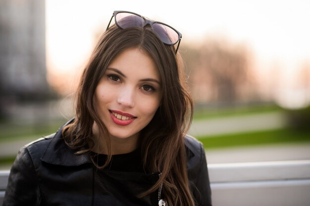 Close portrait of beautiful smiling dark-haired young woman, against summer green park on the sunset