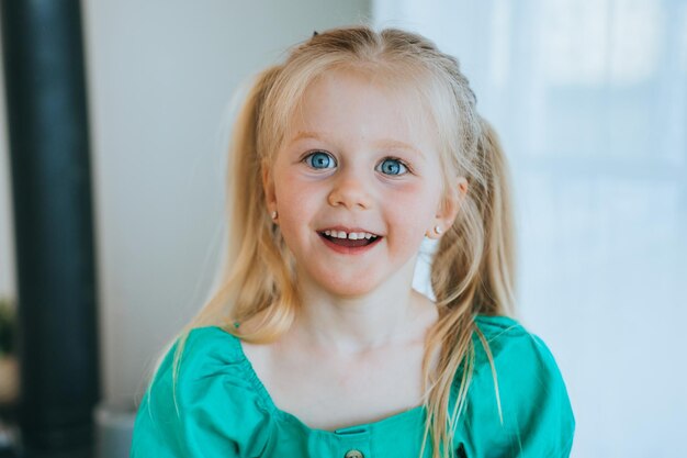 Foto il ritratto ravvicinato della bambina caucasica bionda in vestito verde sorride guarda la macchina fotografica con sorpresa