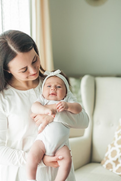 Close portrait of a little cute darkhaired newborn girl in a white suit in the arms of a young mother Motherhood Parent Healthy sleep