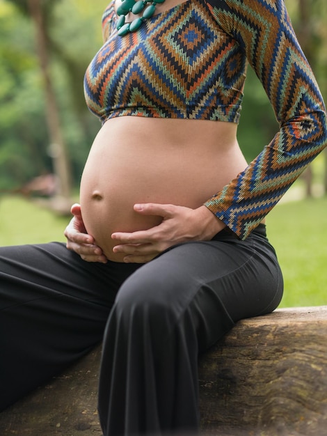 屋外で彼女の腹に触れる妊娠中の現代の若い女性のクローズ