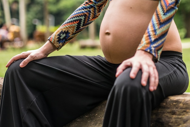 Close of pregnant modern young woman touching her belly outdoors.