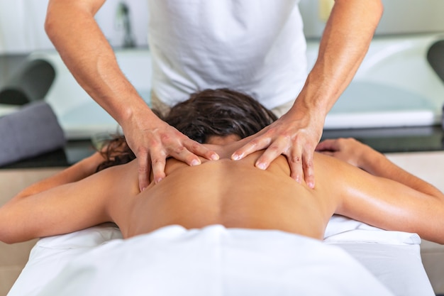 Close rear view of relaxing woman lying face down on massage table receiving a back massage at spa center. Concept of spa.