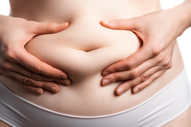 A close shot of female belly, which she pinching a small layer of fat in the belly button.