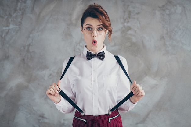 Foto close-uo portret van haar ze mooi uitziende aantrekkelijke mooie mooie schattig verbaasd vrolijk meisjesachtig grappig golvend haar meisje trekken bretels pruilen lippen geïsoleerd op grijze betonnen industriële muur achtergrond