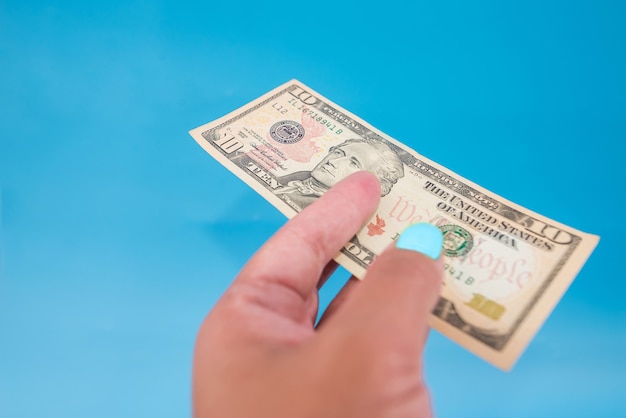 Close-up of 10 dollars in a female hand on a blue background.