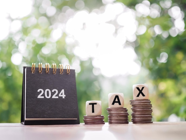 Close up 2024 desk calendar Wooden blocks with the word TAX on stack of coins The concept of saving money for payment tax in New Year 2024