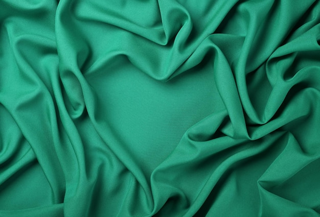 Close up abstract textile background of heart shaped turquoise teal folded pleats of fabric elevated top view directly above