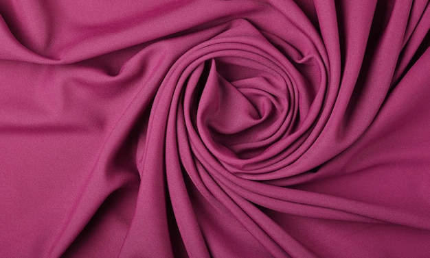 Close up abstract textile background of spiral shaped purple pink folded pleats of fabric, elevated top view, directly above