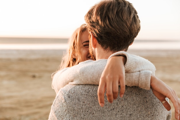 Close-up achteraanzicht van een mooi jong stel dat op het zonnige strand staat en elkaar omarmt