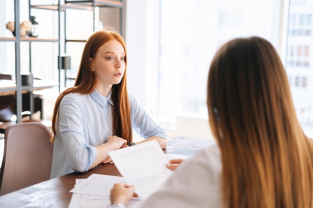 Close-up achteraanzicht van twee jonge zakenvrouwen die nieuwe projectideeën bespreken die aan het bureau tegenover elkaar zitten in de kantoorvergaderruimte