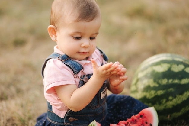 Close up of adorable baby girl eat watermelon stylish baby in denim dress beautiful child eat fruit