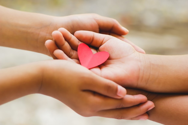Photo close up of adult and child hands holding red heart.