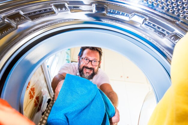 Foto primo piano di un uomo adulto che pulisce e mette i vestiti all'interno della lavatrice - uomo che fa i lavori domestici