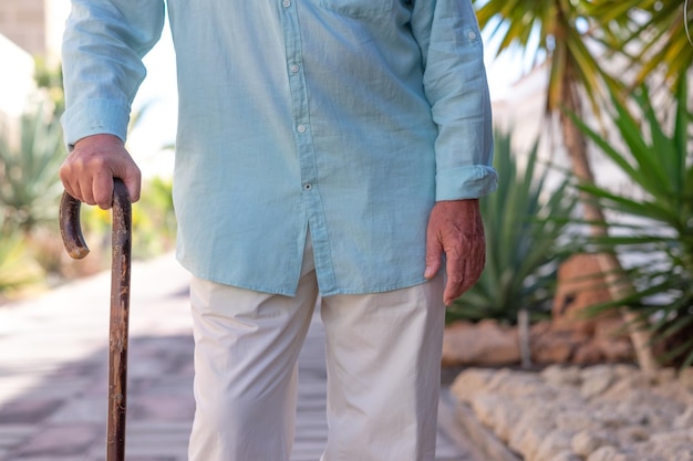 Photo close up on adult mature senior man walking with the help of a stick retired people holding hand on wooden cane aged grandfather outdoor in a tropical garden elderly people health care concept