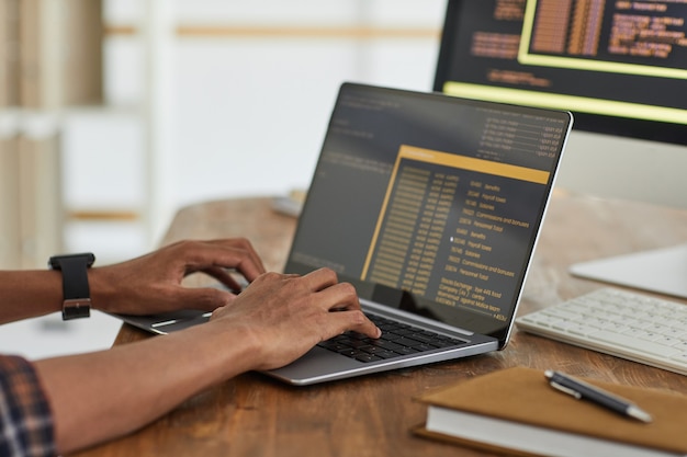 Close up of African-American computer programmer typing on keyboard with black and orange programming code on laptop screen, copy space