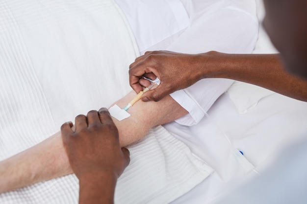 Close up of African-American doctor setting up IV drip while treating patient in hospital, copy space