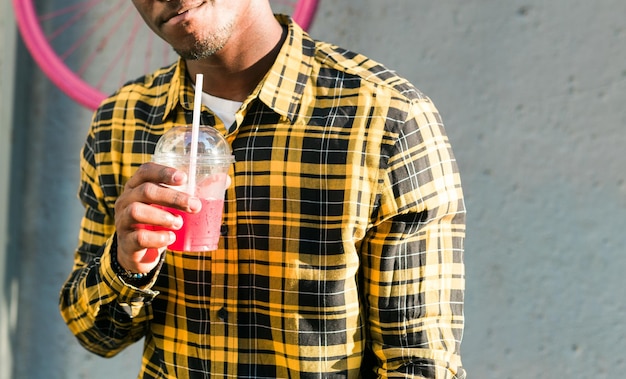 Foto chiuda sul ragazzo afroamericano in abbigliamento casual che tiene fresco il fondo urbano di estate del cocktail tropicale