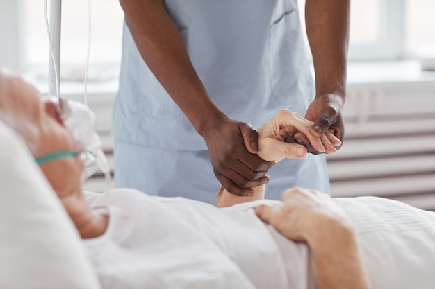 Photo close up of african-american male nurse holding hand of senior man in hospital and comforting him, copy space