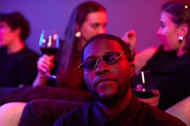 Close up of african american man wearing colored sunglasses at\
party lit by neon lights