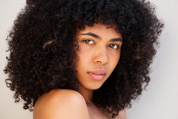 Chiuda sulla donna afroamericana con capelli ricci contro fondo bianco