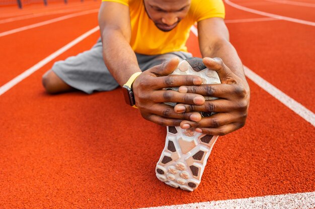 Photo close up african american young male sitting at stadium stretching legs on bright background