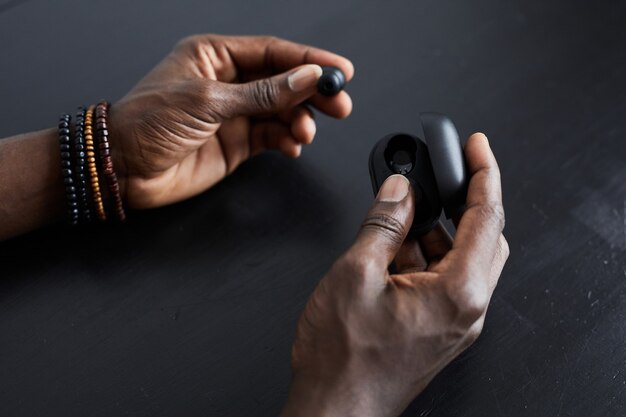 Close-up of African man sitting at the table taking out the wireless headphones for use