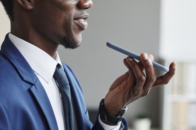 Close-up of African man in suit holding mobile phone and talking on it or recording an audio message