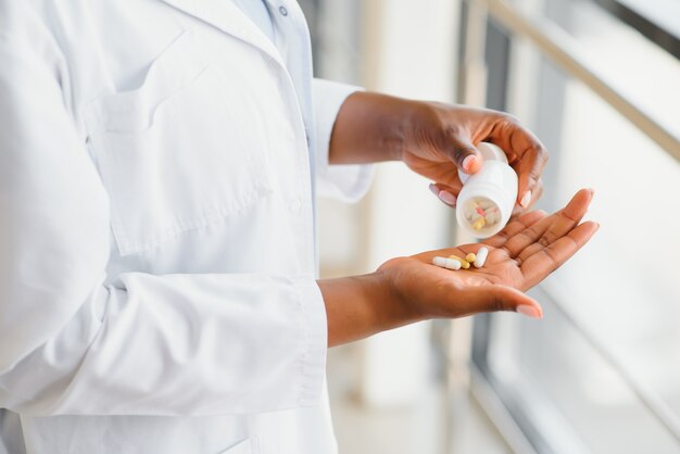 Афро-американский врач крупным планом показывает таблетки и стакан воды перед камерой