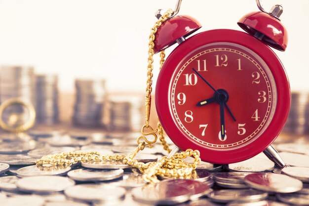 Photo close-up of alarm clock on coins with gold chain at table