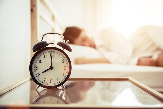 Photo close-up of alarm clock on table with young woman sleeping on bed at home