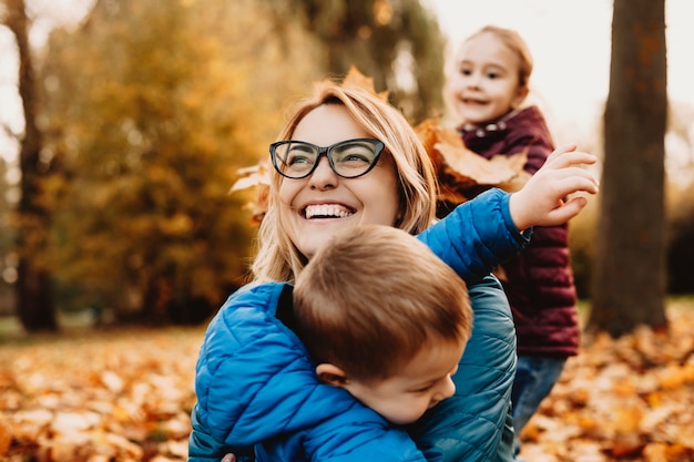 彼女の子供たちと屋外で遊んでいる間笑っている驚くべき若い母親のクローズアップ。公園で笑っている幼い息子を抱き締める素敵な母親。