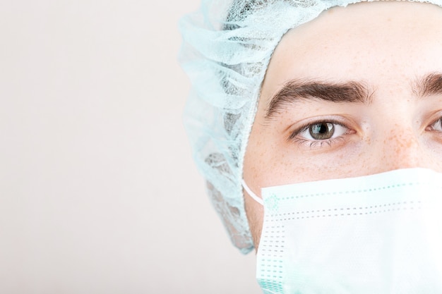 Close up of american male doctor or surgeon in protective facial mask over grey