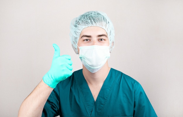 Close up of american male doctor or surgeon rise up his finger in protective facial mask over grey