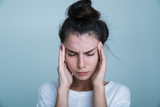 Close up of an annoyed young woman wearing t-shirt isolated over blue background, having a headache