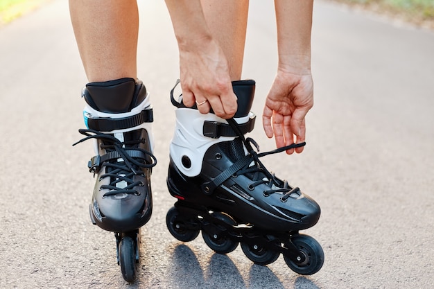 Close-up of an anonymous woman hands fixing laces on roller blades during skating, unknown female on road in summer park, rollerblading, active lifestyle.